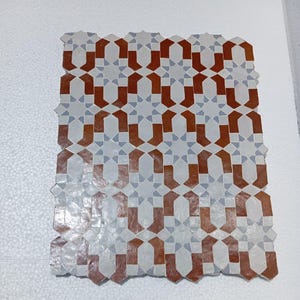 May include: A rectangular arrangement of interlocking tiles featuring a geometric pattern in terracotta orange, light grey, and white. The design consists of repeating star and cross shapes that create a continuous, symmetrical mosaic layout.