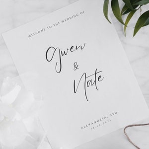 Puede incluir: Un letrero de bienvenida de boda blanco con texto negro. Dice "Welcome to the Wedding of Gwen & Nate." También incluye la ubicación y la fecha: Alexandria, SYD 12.10.2025.