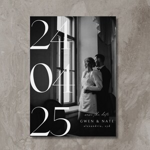 May include: Black and white wedding save the date card with a photo of a couple standing in front of a window. The date "24 04 25" is printed in large white font. The text "save the date" is printed in small white font. The names "GWEN & NATE" are printed in white font. The location "alexandria, syd" is printed in white font.