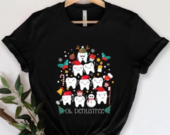 May include: Black t-shirt featuring a festive design of smiling teeth decorated as a Christmas tree. The teeth wear Santa hats and are surrounded by snowflakes, ornaments, and the text "Oh Dentistree".