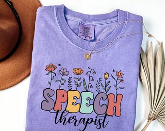 May include: Purple t-shirt with a floral design and the text "SPEECH therapist" in colorful letters.