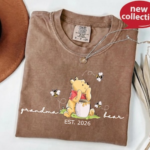A brown t-shirt with a Winnie the Pooh graphic and the text "Grandma Bear" printed on it, along with a necklace and a hat.