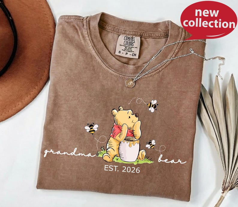 A brown t-shirt with a Winnie the Pooh graphic and the text "Grandma Bear" printed on it, along with a necklace and a hat.