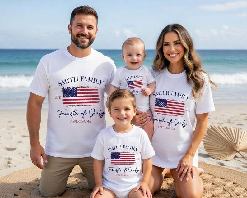 A family of four, consisting of a father, mother, and two children, posing together on a beach. They are all wearing matching white t-shirts with the text "Smith Family Fourth of July Cape Cod, MA" printed on them.