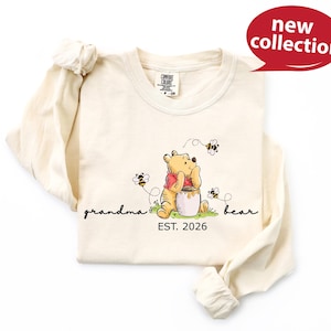 A white long-sleeved t-shirt with a Winnie the Pooh graphic and the text "Grandma Bear" printed on it.