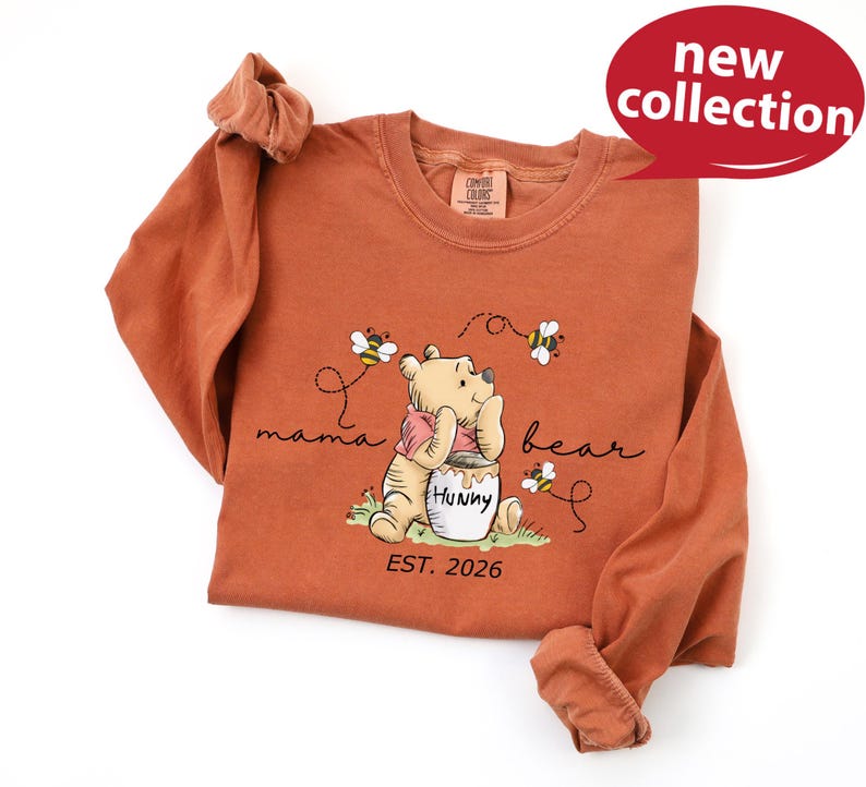 A red long-sleeved t-shirt with a Winnie the Pooh graphic and text, along with a red speech bubble that says "new collection".