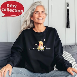 A smiling woman wearing a black sweatshirt with a Winnie the Pooh design sits on a couch.