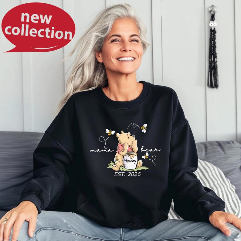 A smiling woman wearing a black sweatshirt with a Winnie the Pooh design and text.