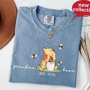 A blue t-shirt with a Winnie the Pooh graphic and the text "grandma bear" printed on it, along with a necklace and a brown hat.