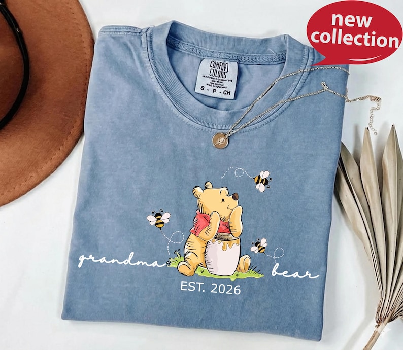 A blue t-shirt with a Winnie the Pooh graphic and the text "grandma bear" printed on it, along with a necklace and a brown hat.