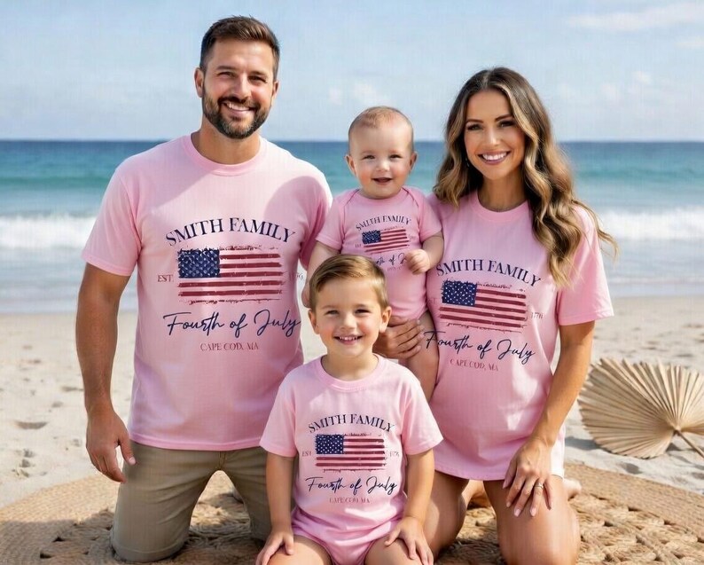A family of four, consisting of a man, a woman, and two children, posing together on a beach. They are all wearing matching pink t-shirts with the text "Smith Family Fourth of July Cape Cod, MA" printed on them.