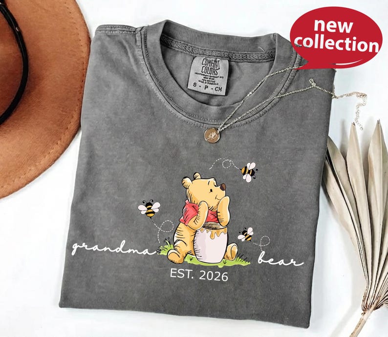 A gray t-shirt with a Winnie the Pooh graphic and the text "Grandma Bear" printed on it, along with a necklace and a brown hat.