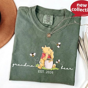 A green t-shirt with a Winnie the Pooh design and the text "Grandma Bear" printed on it, along with a small charm necklace.