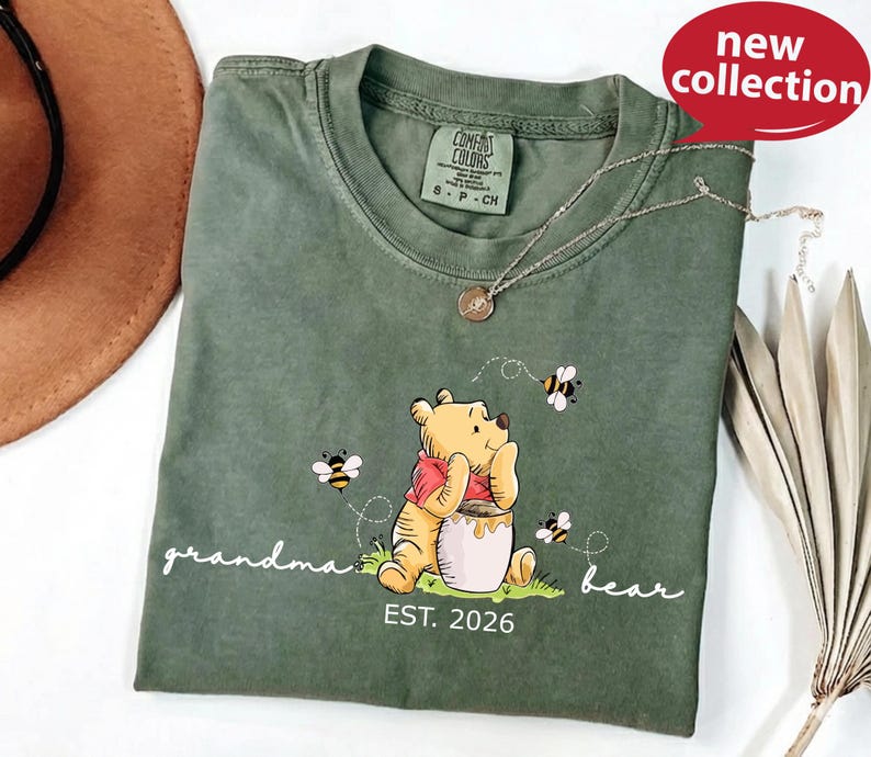 A green t-shirt with a Winnie the Pooh design and the text "Grandma Bear" printed on it, along with a small charm necklace.