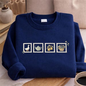 A navy blue sweater with a decorative design of four postage stamps on it, along with a cup of coffee and a small plant in the background.