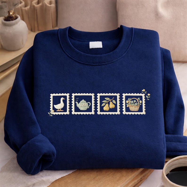 A navy blue sweater with a decorative design of four postage stamps on it, along with a cup of coffee and a small plant in the background.
