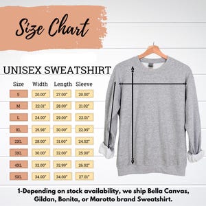 Puede incluir: Una sudadera unisex gris claro colgada de una percha de madera. Se muestra una tabla de tallas, que muestra las medidas en pulgadas de ancho, largo y largo de manga. La tabla incluye tallas de la S a la 5XL. El texto "Size Chart" est&aacute; en la parte superior.