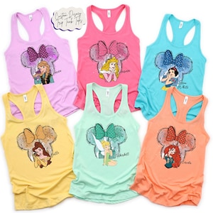 May include: Six brightly coloured tank tops with Disney character designs. Each vest top has a racerback style and a graphic of a Disney character inside a Mickey Mouse ear outline. The text "Custom Disney Trip Tank Tops" is at the top.