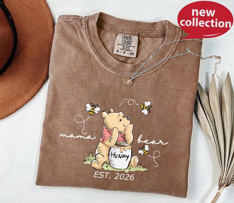 A brown t-shirt with a Winnie the Pooh-themed design, including the character Huckleberry Bear, is displayed on a white surface.