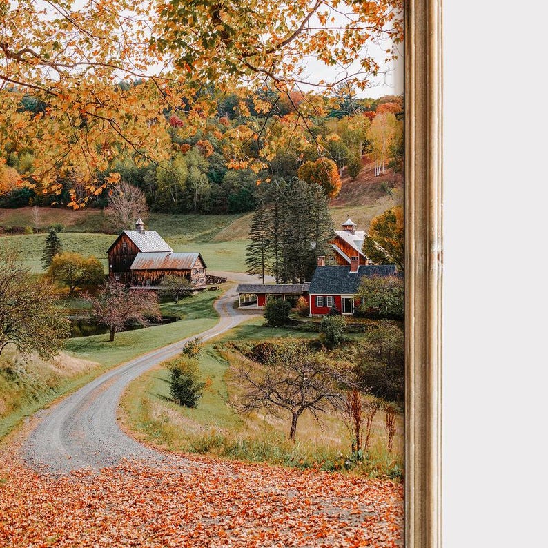 May include: A winding dirt road leads to a red farmhouse with a white trim and a green roof. The farmhouse is surrounded by trees with colorful fall foliage.