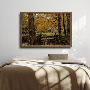 May include: A rustic wooden cabin nestled in a forest with vibrant autumn foliage. The cabin has a wooden fence and is surrounded by trees with yellow, orange, and red leaves.