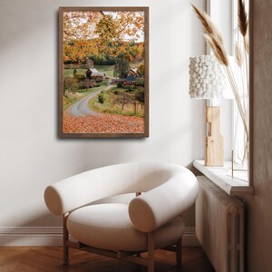 May include: A framed photograph of a country road winding through a field of autumn leaves. The road leads to a red barn and a farmhouse in the distance. The trees are a mix of green and yellow.