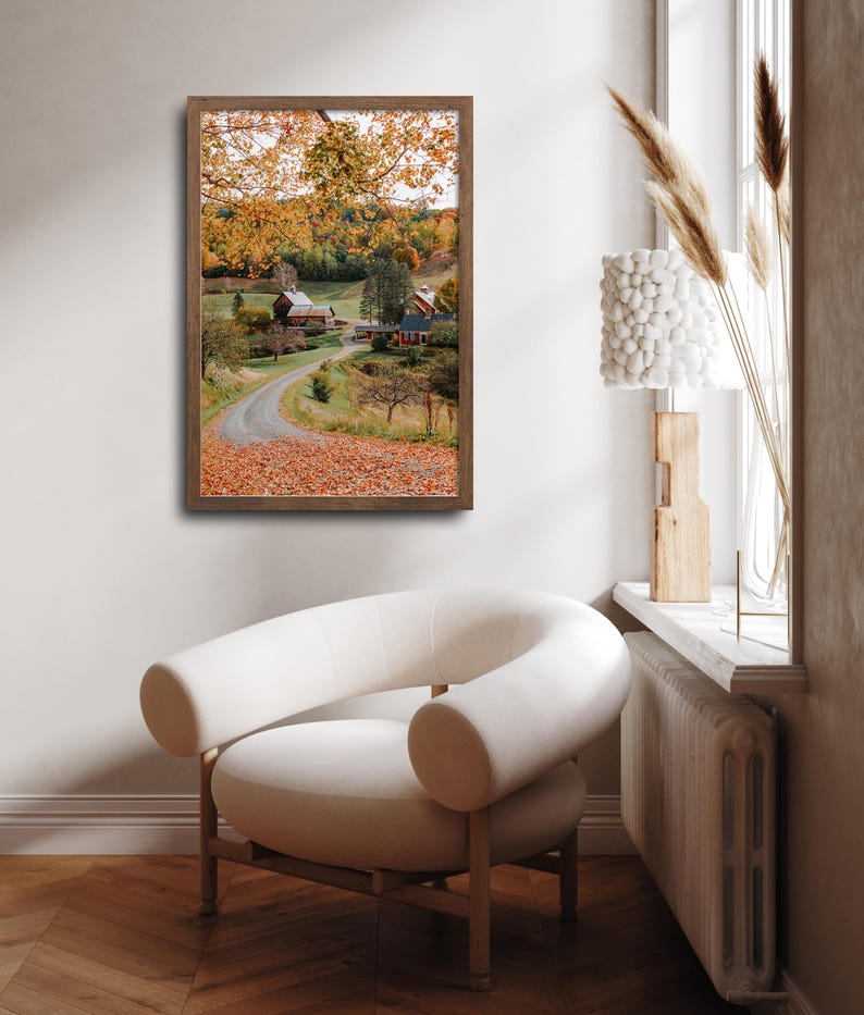 May include: A framed photograph of a country road winding through a field of autumn leaves. The road leads to a red barn and a farmhouse in the distance. The trees are a mix of green and yellow.