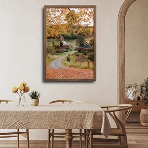May include: A framed photograph of a winding country road leading to a farmhouse in a rural setting. The trees are in autumn colors, with shades of yellow, orange, and red. The road is lined with fallen leaves.