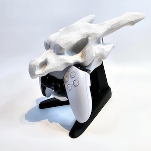 May include: A white 3D printed dragon head controller stand with a white game controller. The stand is black and has a base.