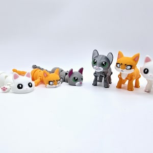 May include: Five small plastic cat figurines. One is white, one is gray, one is orange, and two are white with orange accents. The cats are all in different poses.