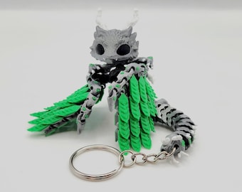 May include: A gray and green dragon keychain with a silver chain. The dragon has a green leafy tail and wings.