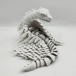 Puede incluir: Una escultura de dragón blanca impresa en 3D con un diseño detallado y escamoso. El dragón está enroscado en una postura defensiva, con la cabeza metida en el cuerpo.