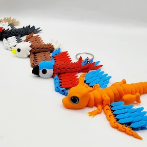 May include: A set of six colorful, 3D printed animal keychains. The keychains are made of plastic and feature a variety of animals, including a bird, a dragon, and a parrot. The keychains are all attached to metal rings.