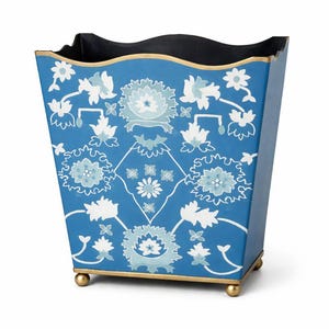 May include: A blue waste bin with a floral pattern in white and light blue. The bin has a gold trim and sits on small gold feet. The interior is black.