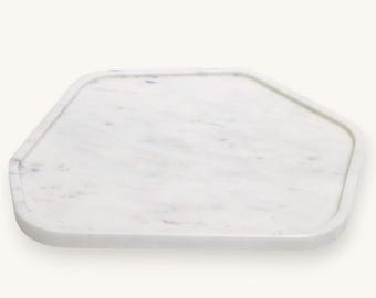 May include: A white marble serving tray with an unusual, geometric form. The tray features a gently raised edge and a polished finish. The marble displays delicate grey veining. Suitable for serving appetizers or displaying decorative items.