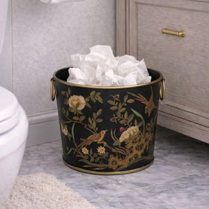 Può includere: Cestino nero con un design floreale e di uccelli. Il cestino ha manici e finiture color oro. L'interno è pieno di fazzoletti bianchi. Il cestino è in un ambiente bagno.