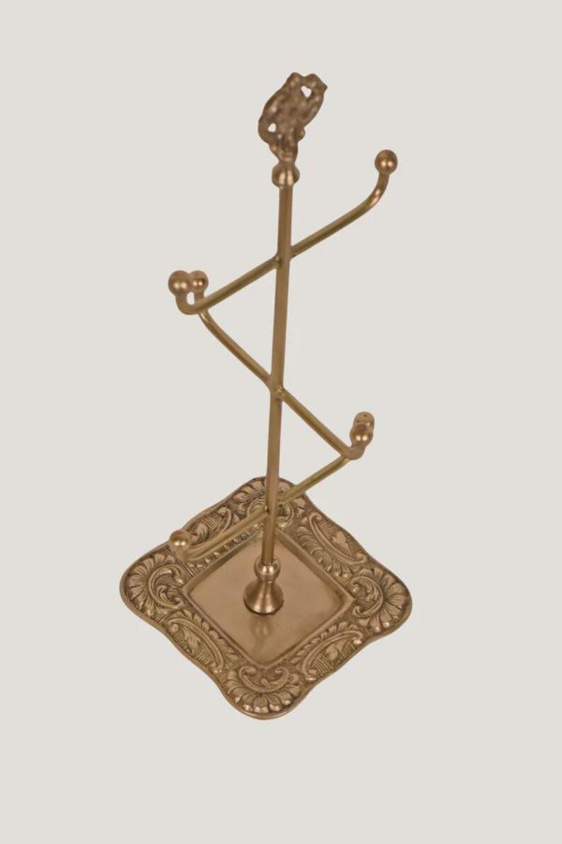 Suporte artesanal em latão para exibição de joias e acessórios, com ponteira ornamentada e múltiplos ganchos. imagem 5