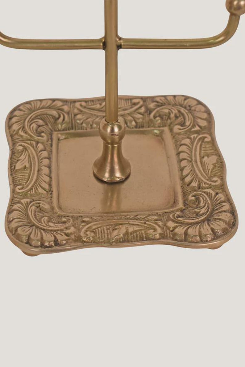 Suporte artesanal em latão para exibição de joias e acessórios, com ponteira ornamentada e múltiplos ganchos. imagem 4
