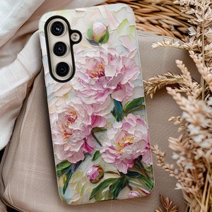 May include: A phone case with a floral design featuring pink peonies and green leaves. The case has a white background and a textured look.