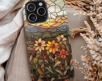 May include: A phone case with a stained glass design featuring a sunset over mountains and flowers. The case has a black camera cutout and a clear background.