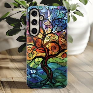 May include: A colorful phone case with a stained glass design of a tree with swirling branches. The case has a black background and a multi-colored tree with blue, green, orange, and yellow accents.