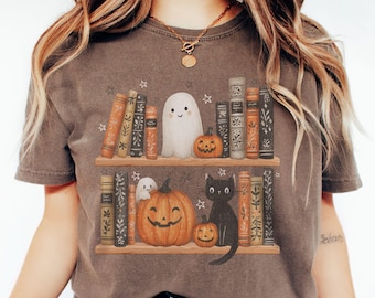 以下が含まれることがあります： ハロウィーンをテーマにしたグラフィックが特徴の茶色のTシャツ。デザインには、本棚、笑顔の幽霊、カボチャ、黒猫が含まれています。シャツはヴィンテージで、少し色あせた外観をしています。