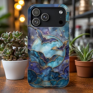 May include: A phone case featuring a Halloween-themed design. The case has a blue and purple watercolor background with gold outlines. The design includes bats, a full moon, and stars. The case has three camera lenses.