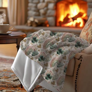 May include: A soft, cream-colored blanket with a pattern of rainbows, clouds, shamrocks, and hearts in pastel colors. The blanket is draped over a chair in front of a fireplace, creating a cozy, inviting scene.