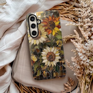 May include: A phone case with a stained glass design featuring sunflowers in shades of yellow, orange, and brown. The case has a cutout for a triple lens camera.