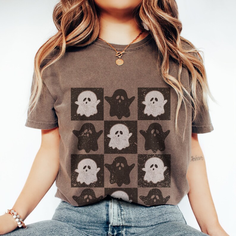 May include: A brown t-shirt with a checkered pattern of white and black ghosts. The ghosts are in a grid pattern and have a vintage look.