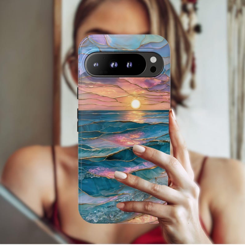 May include: A phone case featuring a sunset over the ocean design. The case has a colorful, abstract design with shades of blue, pink, and gold. The phone case is held up in front of a person.
