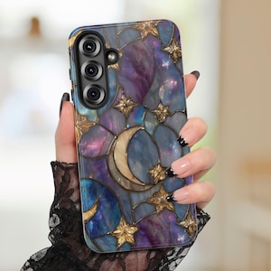 May include: A phone case with a celestial design featuring a crescent moon and stars in gold against a backdrop of blue and purple hues. The case has a glossy finish and a camera cutout.