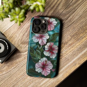 May include: A phone case with a stained glass design featuring pink and white hibiscus flowers on a teal background.
