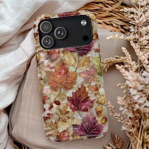 May include: A smartphone case featuring a decorative mosaic pattern of autumn leaves in shades of red, orange, gold, and brown, interspersed with small acorns and berries, set against a pearlescent white background with a black camera module.